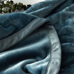 Gros plan sur une couverture ou un plaid doux et texturé de couleur vert foncé, avec des plis et des reflets miroitants, créant une ambiance cocooning et chaleureuse.