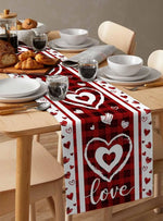 Une table dressée avec des assiettes, des verres et des pâtisseries, le tout surplombé d'un chemin de table rouge décoré de coeurs blancs et du mot "love".