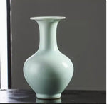 Vase en céramique de couleur vert pâle avec une forme élégante et épurée, posé sur une surface sombre.