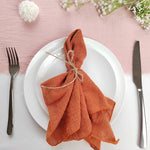 Une belle nappe rose pastel avec une serviette roulée en nœud de couleur rouille, accompagnée d'ustensiles de table, crée une table élégante et chaleureuse.