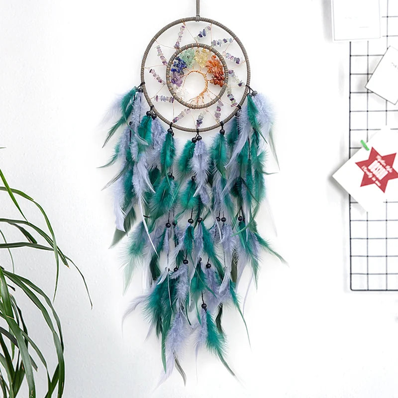 Un attrape-rêves décoratif composé d'un anneau entouré de plumes vertes, bleues et grises, avec un soleil multicolore en son centre, suspendu par un fil.