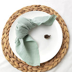 Un plat en céramique blanche posé sur un dessous-de-plat tressé en fibres naturelles, avec un élégant linge de table vert pastel et un cône de pin.