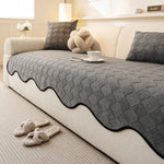 Coussins et couverture en gris foncé sur un canapé beige, avec tasse de café et décorations.