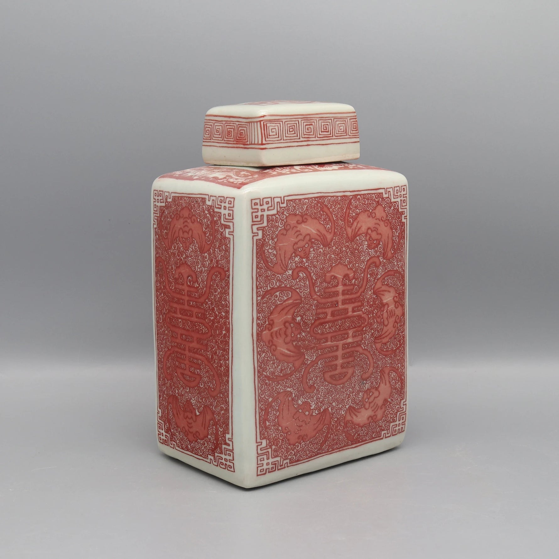 Un vase en céramique décoré de motifs asiatiques élégants et complexes dans des tons rouges et crème.