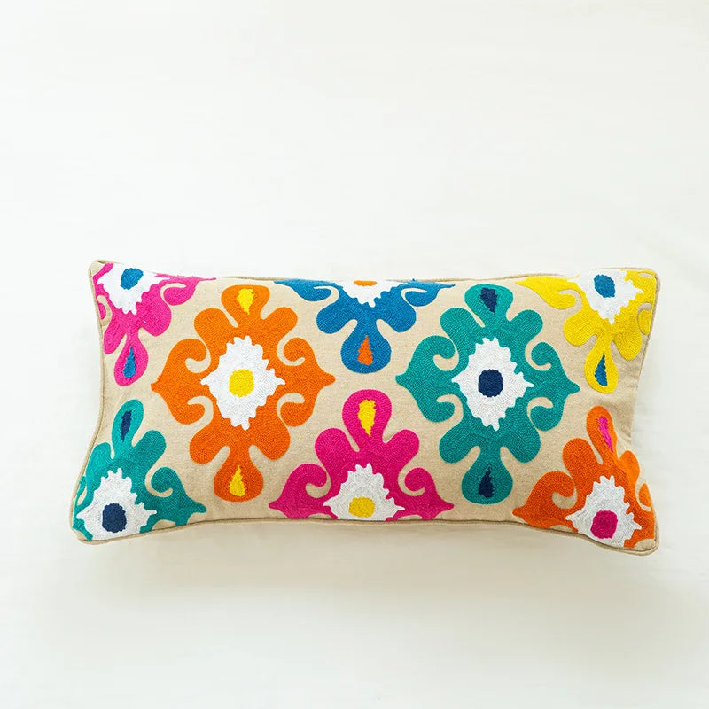 Coussin décoratif coloré avec des motifs floraux et géométriques lumineux sur un fond beige.