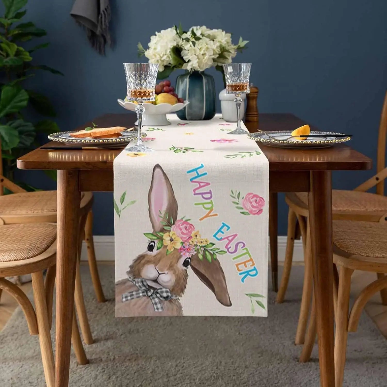 Une table de salle à manger décorée avec un bouquet de fleurs, des verres en cristal et un chemin de table orné d'un joli lapin de Pâques.