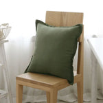 Coussin vert olive posé sur une chaise en bois naturel dans un intérieur lumineux avec des accessoires décoratifs.