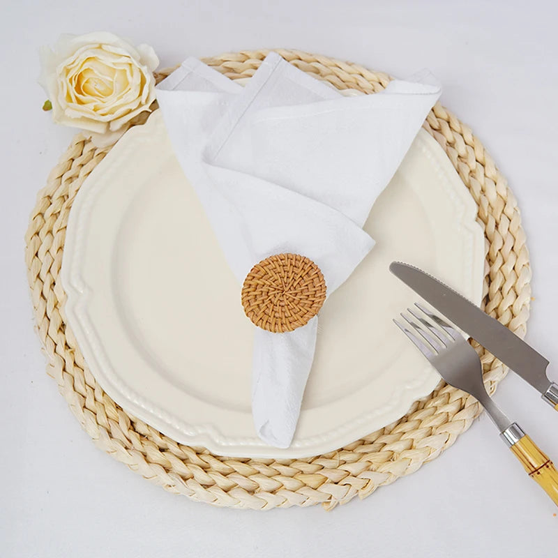 Une belle table de cuisine avec une nappe blanche, une rose jaune et une jolie décoration sur un napperon tressé.