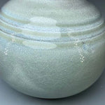 Une élégante urne de porcelaine avec une surface texturée en motifs concentriques irisés, donnant une impression de pureté et de raffinement.