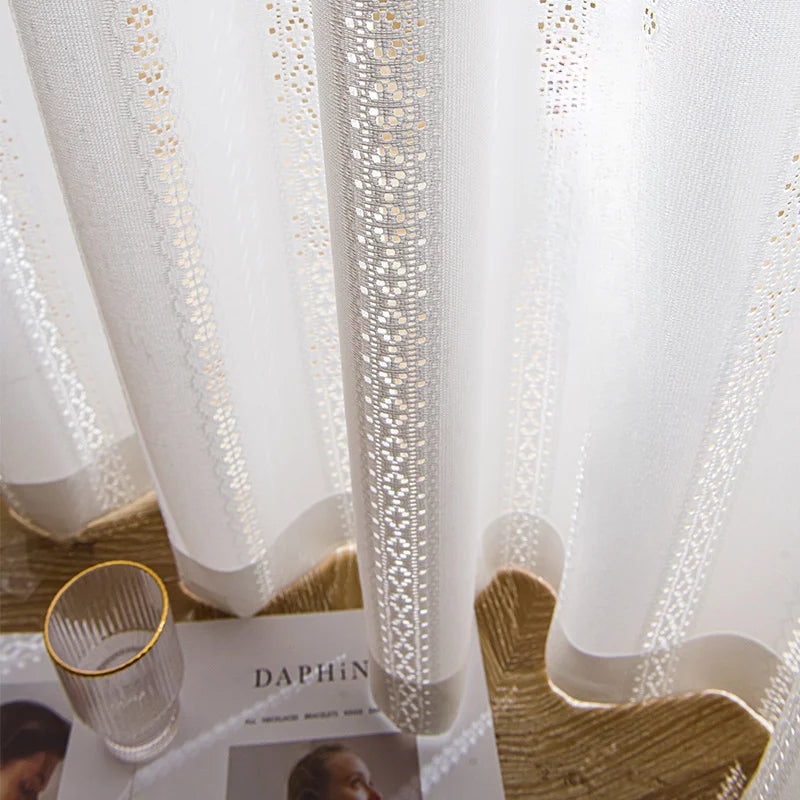 Voilage blanc à ruflette prêt à poser avec broderies délicates, lumière filtrée dans un salon élégant.