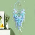 Capteur de rêves en forme de lune bleu et argent avec des plumes blanches et bleues qui pendent, décoré d'un ornement en forme d'étoile scintillante, placé sur une étagère avec des accessoires décoratifs.
