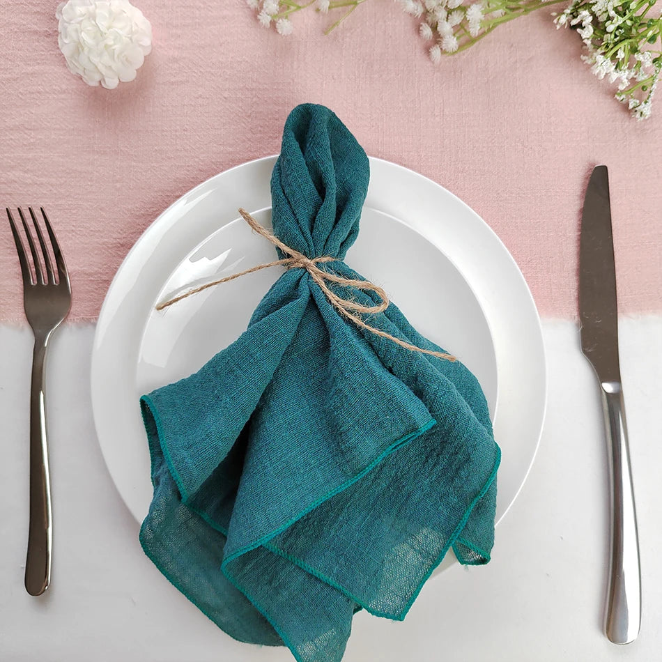 Une assiette blanche avec une serviette verte nouée élégamment, entourée de fleurs fraîches sur un fond rose pâle.