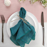 Une assiette blanche avec une serviette verte nouée élégamment, entourée de fleurs fraîches sur un fond rose pâle.