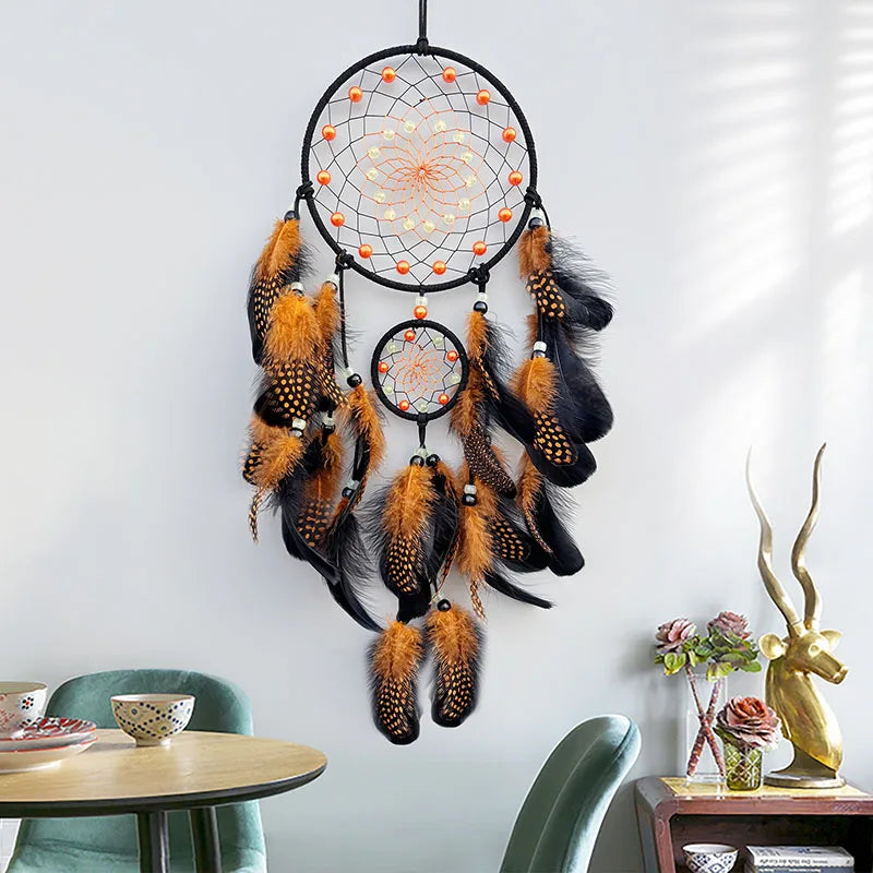 Un attrapeur de rêves ethnique en plumes brunes et noires, orné de motifs géométriques et de perles, suspendu sur un mur avec des décorations en arrière-plan.