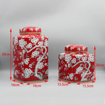 Deux élégants récipients cylindriques rouges décorés de motifs floraux blancs dans un style oriental, présentant des dimensions et des tailles distinctes.
