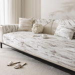Un canapé moelleux avec des motifs abstrait sur le tissu, accompagné de coussins et d'un repose-pieds, créant une atmosphère sereine et relaxante dans le salon.
