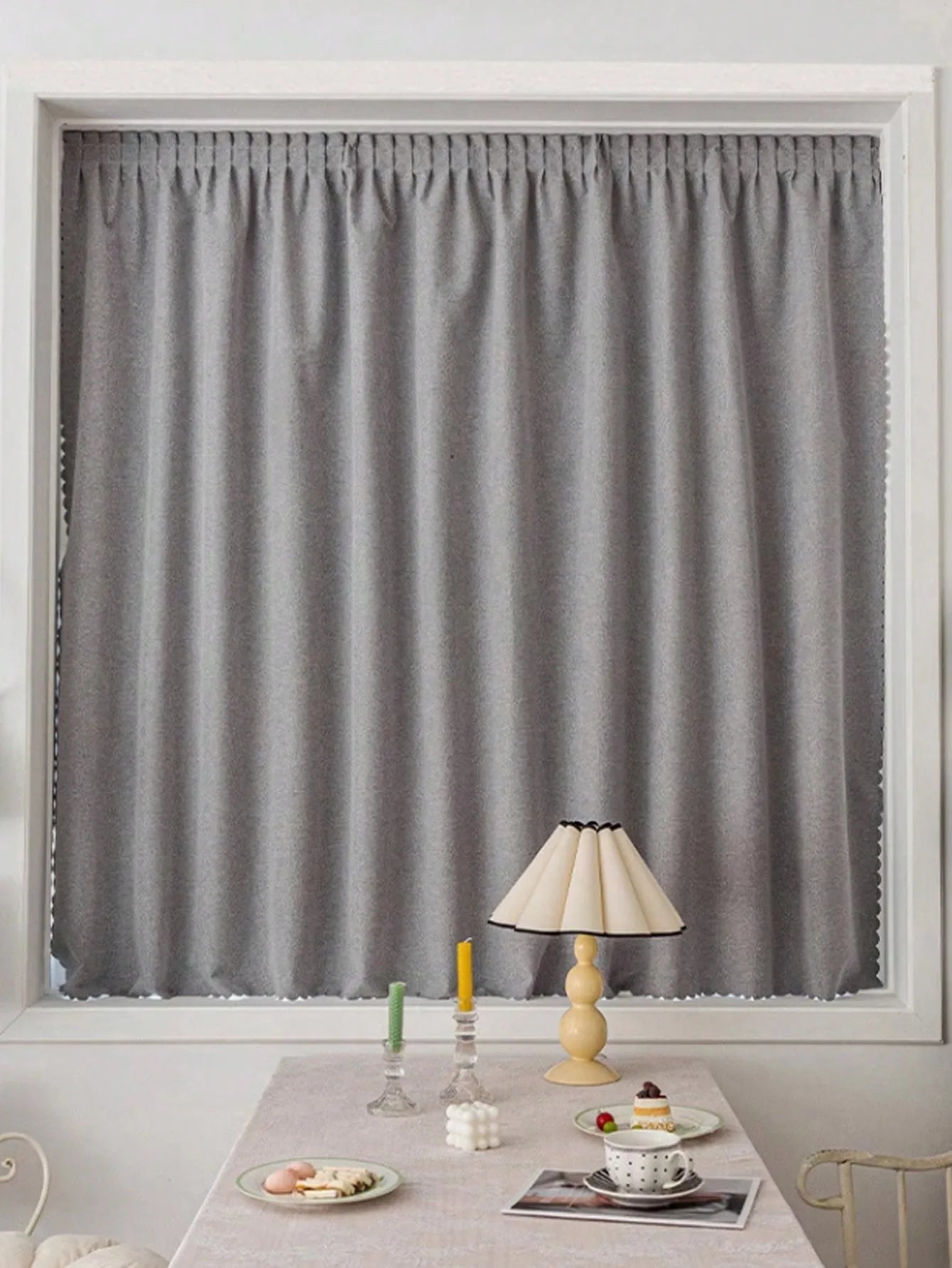 Rideaux modernes gris pour salon, élégamment accrochés dans une fenêtre, offrant une ambiance chaleureuse et tamisée. Idéal pour ajouter une touche de sophistication à votre intérieur. Accompagné d'une table décorée avec une lampe et des accessoires de table colorés. Solution parfaite pour créer un espace de vie accueillant et stylé.