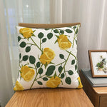 Coussin décoratif motif de roses jaunes et feuilles vertes sur fond blanc.