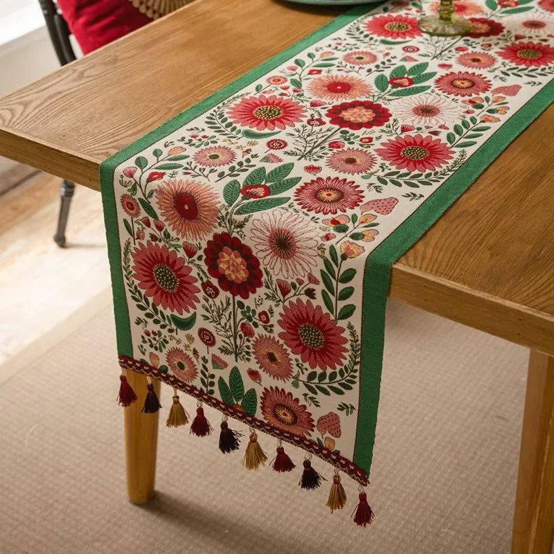 Un chemin de table en coton orné de magnifiques fleurs rouges et vertes, avec des franges et des glands décoratifs aux extrémités, apportant une touche de chaleur et d'élégance à la décoration de la table.