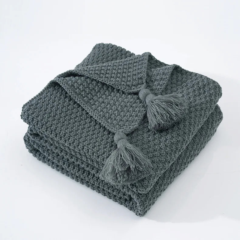 Couverture tricotée grise avec des glands décoratifs.
