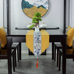 Cette image montre une table à manger dans un intérieur moderne et épuré, avec un chemin de table jaune vif et un superbe décor asiatique comprenant un bonsaï, des vases et une œuvre d'art murale représentant des montagnes brumeuses.