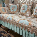 Un canapé orné de motifs floraux élégants dans des tons de vert et beige, avec des ornements dorés sur les accoudoirs et le dossier, créant une ambiance luxueuse et raffinée.