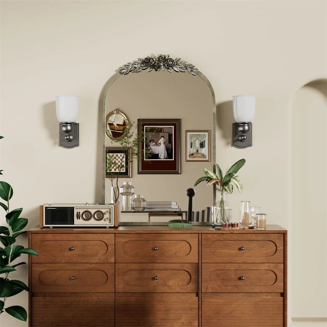 Commode en bois avec un miroir décoratif au-dessus, ornée de plantes vertes et d'éléments de décoration vintage.