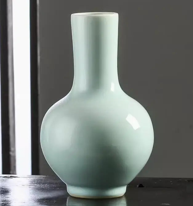 Vase en céramique de couleur vert pâle avec une forme élégante et épurée, posé sur une surface sombre.
