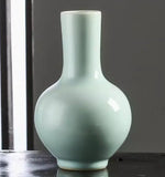 Vase en céramique de couleur vert pâle avec une forme élégante et épurée, posé sur une surface sombre.