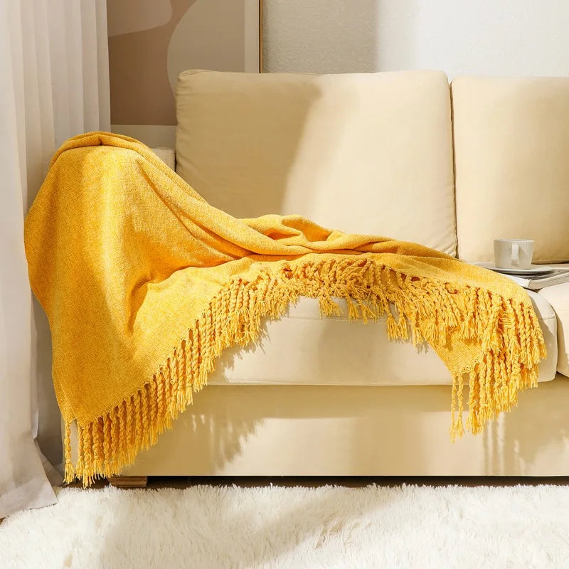 Une couverture en laine de couleur jaune moutarde avec des franges ornemente un canapé clair dans un intérieur lumineux.
