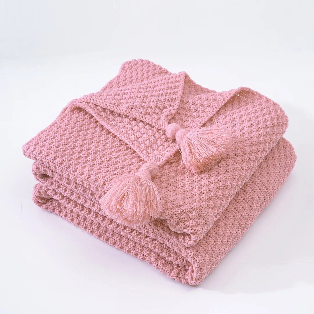 Une couverture tricotée rose avec des pompons, parfaite pour se réchauffer et se détendre.