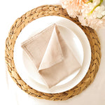 Une élégante table dressée avec une élégante couronne de corde tressée, une serviette blanche soigneusement pliée et une fleur rose.