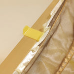 L'image montre une fermeture éclair dorée avec un curseur jaune sur un tissu beige.
