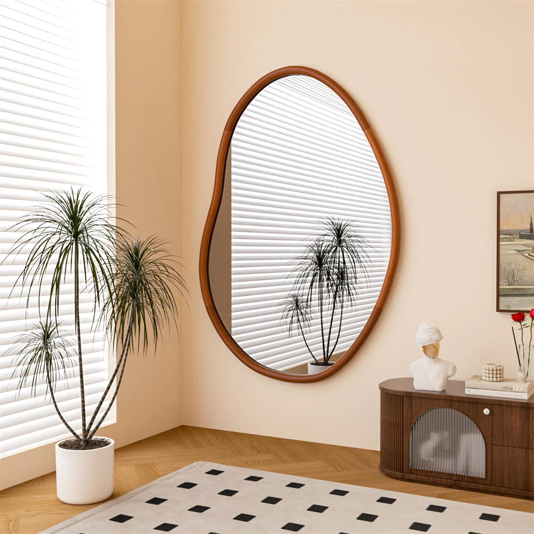 Cette pièce élégante et épurée présente un miroir ovale à cadre en bois, entouré de plantes vertes et d'un meuble vintage, sur un tapis motif géométrique, créant une atmosphère chaleureuse et contemporaine.