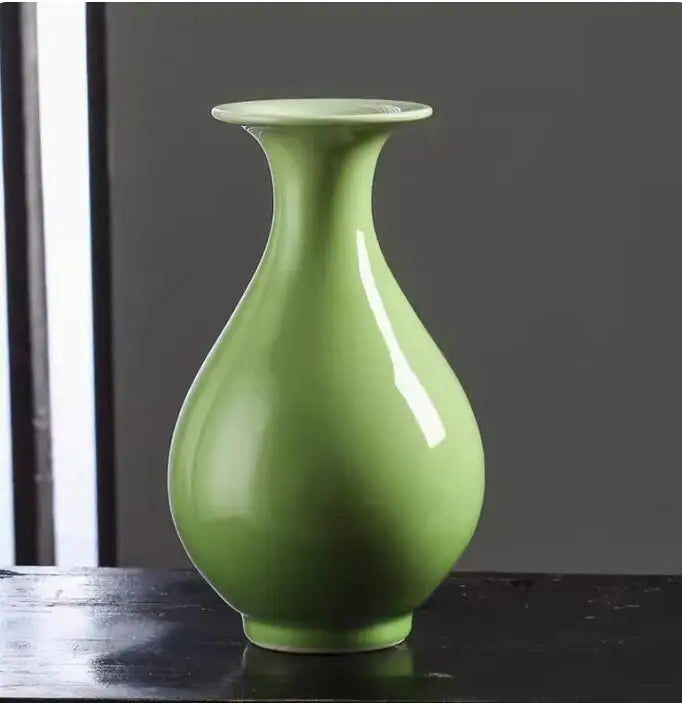 Vase élégant de couleur vert pastel, avec une forme épurée et moderne, placé sur une surface sombre.