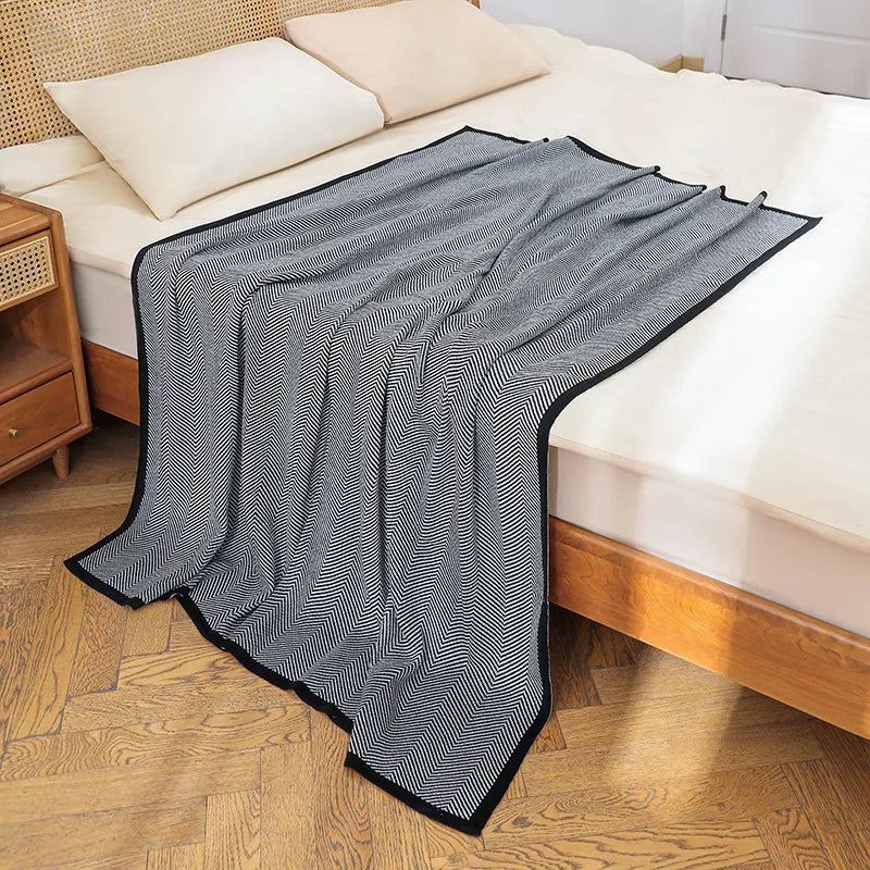 Couverture de lit matelassée à motifs rayés noirs et blancs, posée sur un lit en bois, créant une ambiance élégante et moderne dans la chambre.