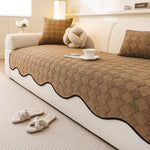 Couvrelit en peluche beige avec motif géométrique et ornements décoratifs, posé sur un canapé blanc dans une pièce confortable et chaleureuse.
