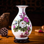Vase en porcelaine blanche orné de fleurs rose et de motifs floraux délicats avec un oiseau en vol, posé sur un socle en bois foncé.