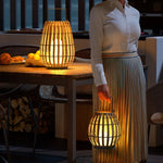 Lampe solaire en rotin entourée de plantes vertes dans un jardin