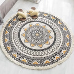Tapis rond orné d'un motif géométrique traditionnel aux couleurs neutres, avec des pompons décoratifs au bord.