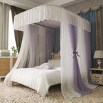 L'image montre un lit à baldaquin magnifiquement décoré avec des rideaux blancs et violets, créant une ambiance élégante et romantique dans la chambre.