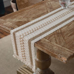 Cette image montre une table en bois avec un chemin de table tissé en couleurs beige et blanches, créant un motif décoratif intéressant sur la surface de la table.