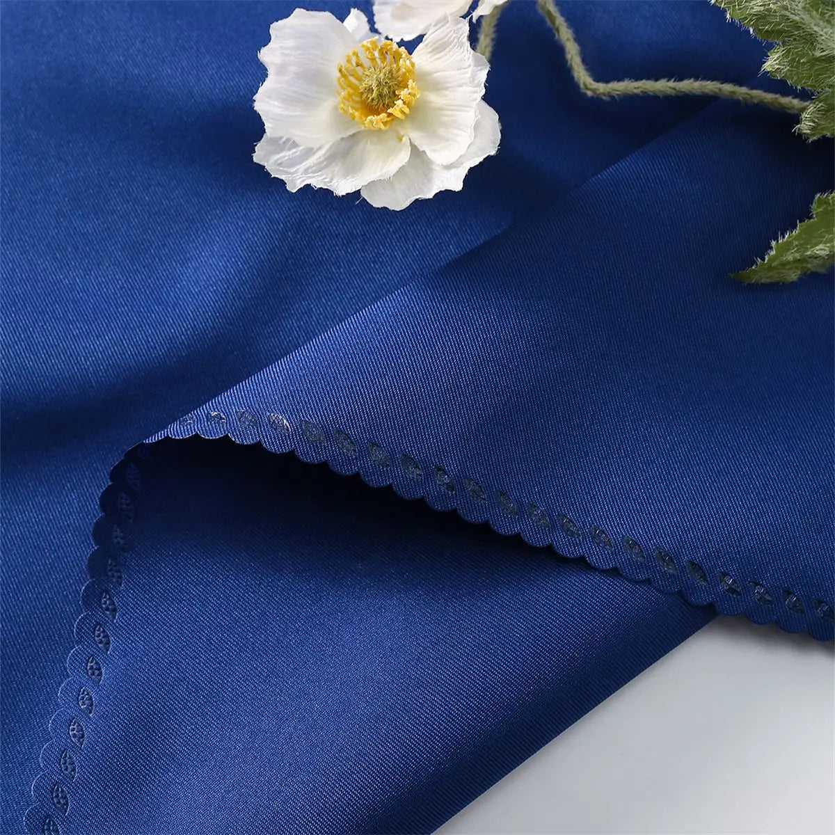 Une élégante fleur blanche avec un pistil jaune repose sur une surface bleue lisse et brillante.