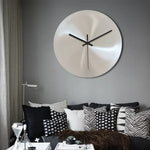 Horloge murale industrielle argentée minimaliste accrochée sur un mur de salon moderne