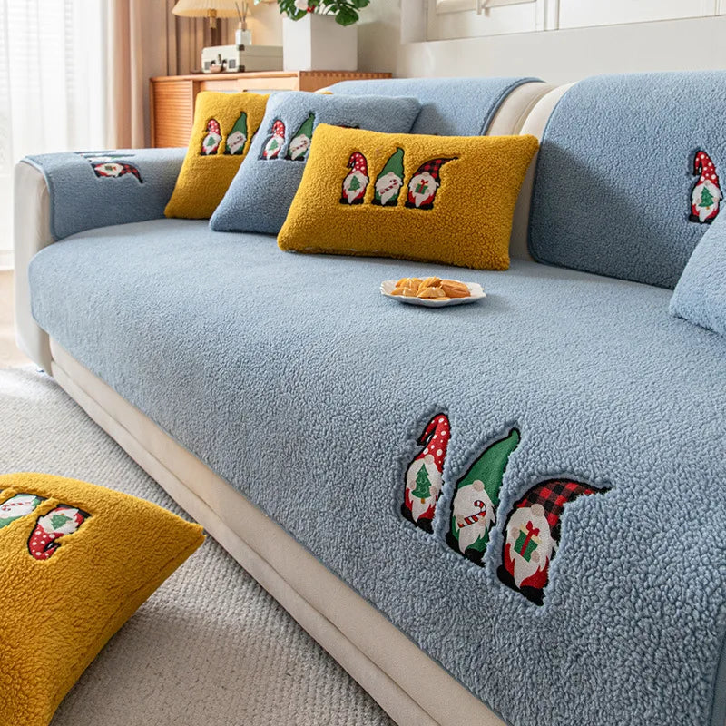 Un canapé gris confortable décoré de coussins jaunes ornés de motifs de lutins saisonniers, avec des frites sur un plaid à proximité, créant une ambiance chaleureuse et festive dans le salon.