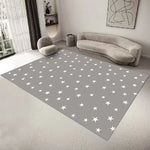 Le tapis au sol présente un motif de nombreuses étoiles blanches sur un fond gris, créant un style épuré et moderne dans cette pièce avec un canapé gris et d'autres éléments de décoration.