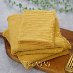 Serviettes en tissu éponge jaune vif, pliées avec soin sur une planche en bois.
