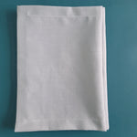 Serviette de table blanche pliée sur fond turquoise.
