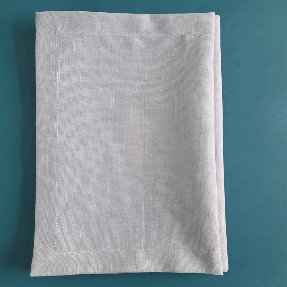 Serviette de table blanche pliée sur fond turquoise.