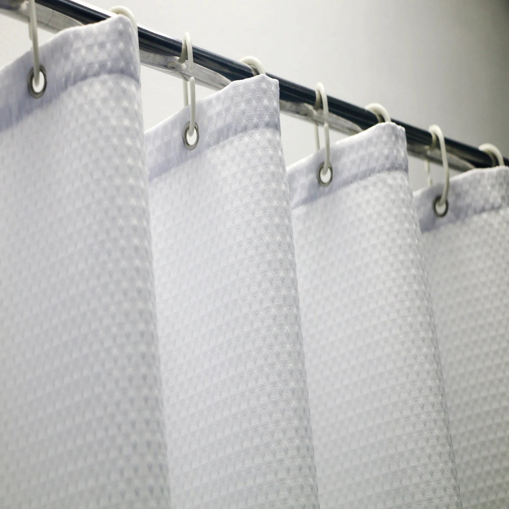 Rideau de douche blanc, accessoire de salle de bain et élément de plomberie, apportant une touche moderne et élégante à l'intérieur de la salle de bain grâce à son design élégant et sa finition métallique.